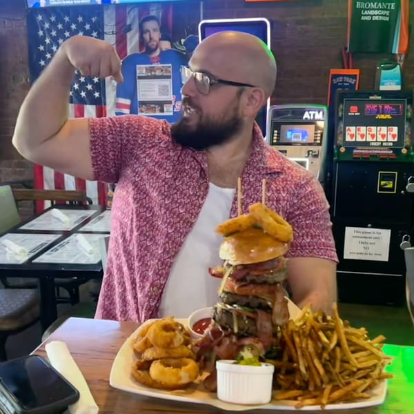 Man flexing his arm next to a giant burger, onion rings, and fries at a bar.