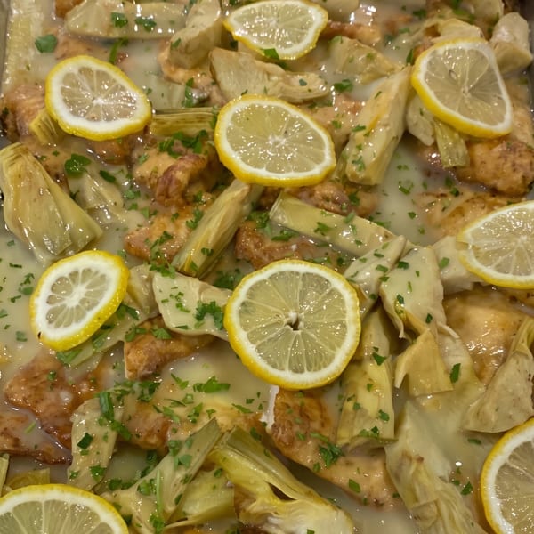 Chicken and artichoke hearts in a lemon sauce, garnished with fresh parsley and lemon slices.
