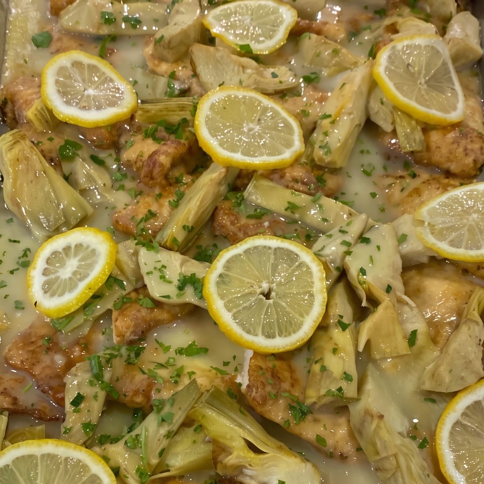 Chicken and artichoke hearts in a lemon sauce, garnished with fresh parsley and lemon slices.