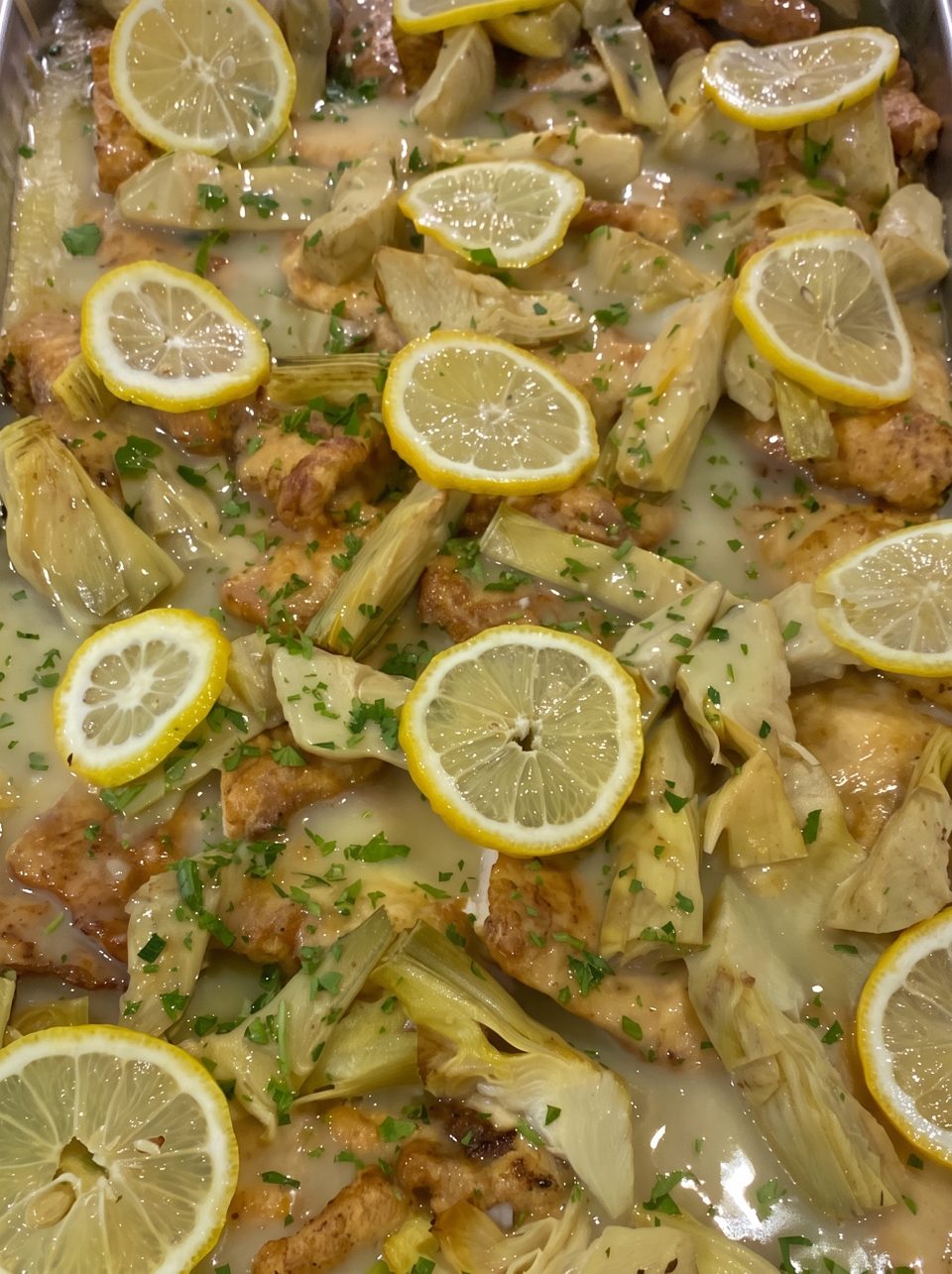Chicken and artichoke hearts in a lemon sauce, garnished with fresh parsley and lemon slices.