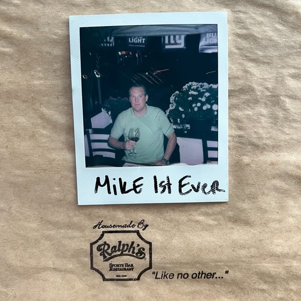 A polaroid of a man in a green shirt holding a glass of red wine, with "Mike 1st Ever" written below.