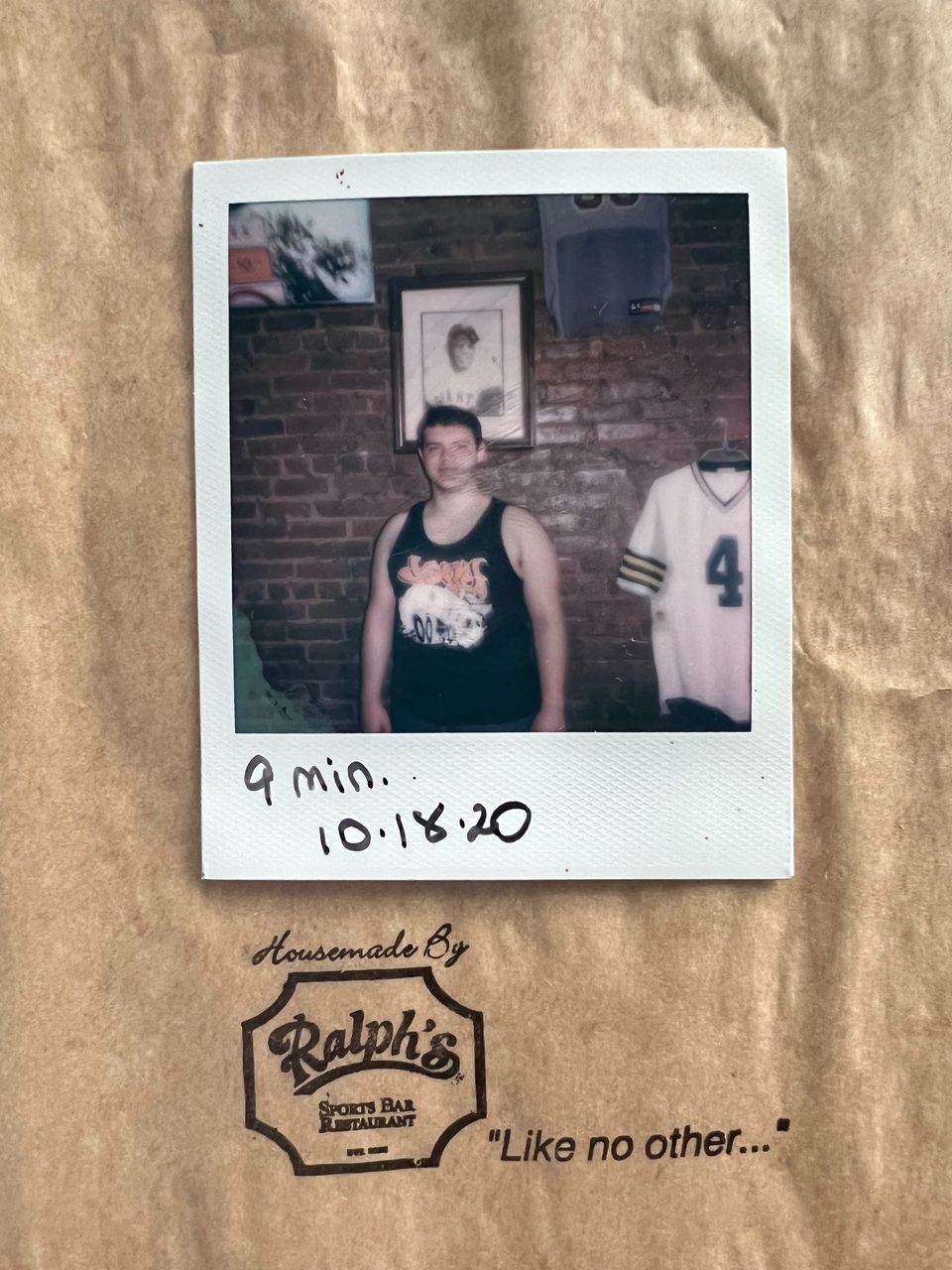 Polaroid photo of a man in a tank top against a brick wall, with a Ralph's Sports Bar logo.