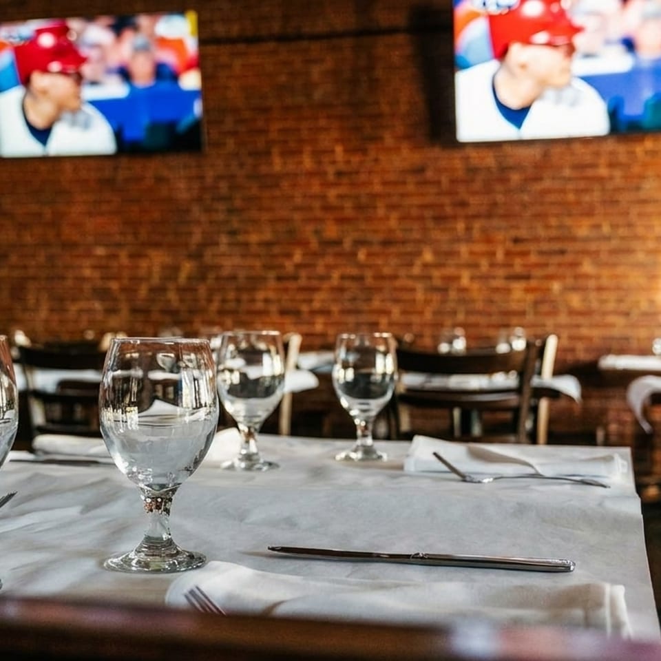 Restaurant dining room with set tables, brick wall, and two TVs showing a baseball game.