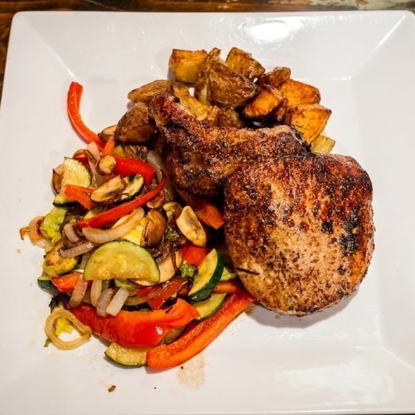 Grilled pork chops with roasted potatoes and sautéed vegetables on a white plate.