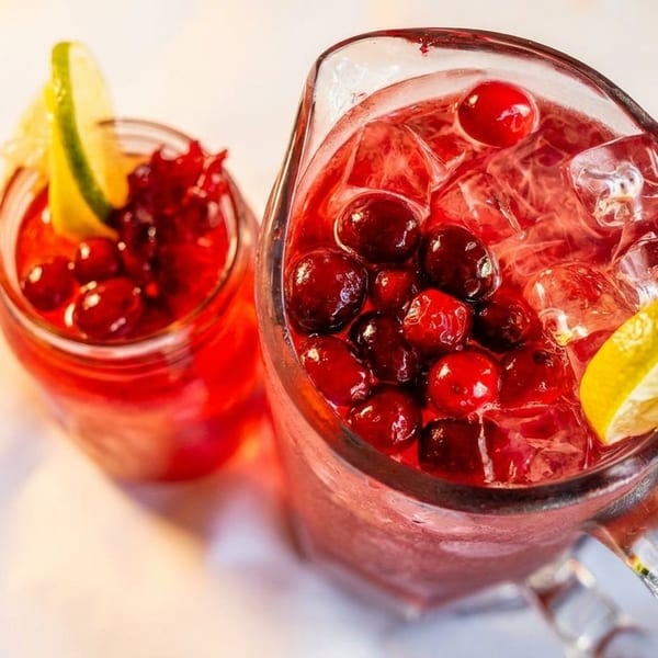 Two glasses of red cranberry drink with ice, garnished with lime and lemon slices.