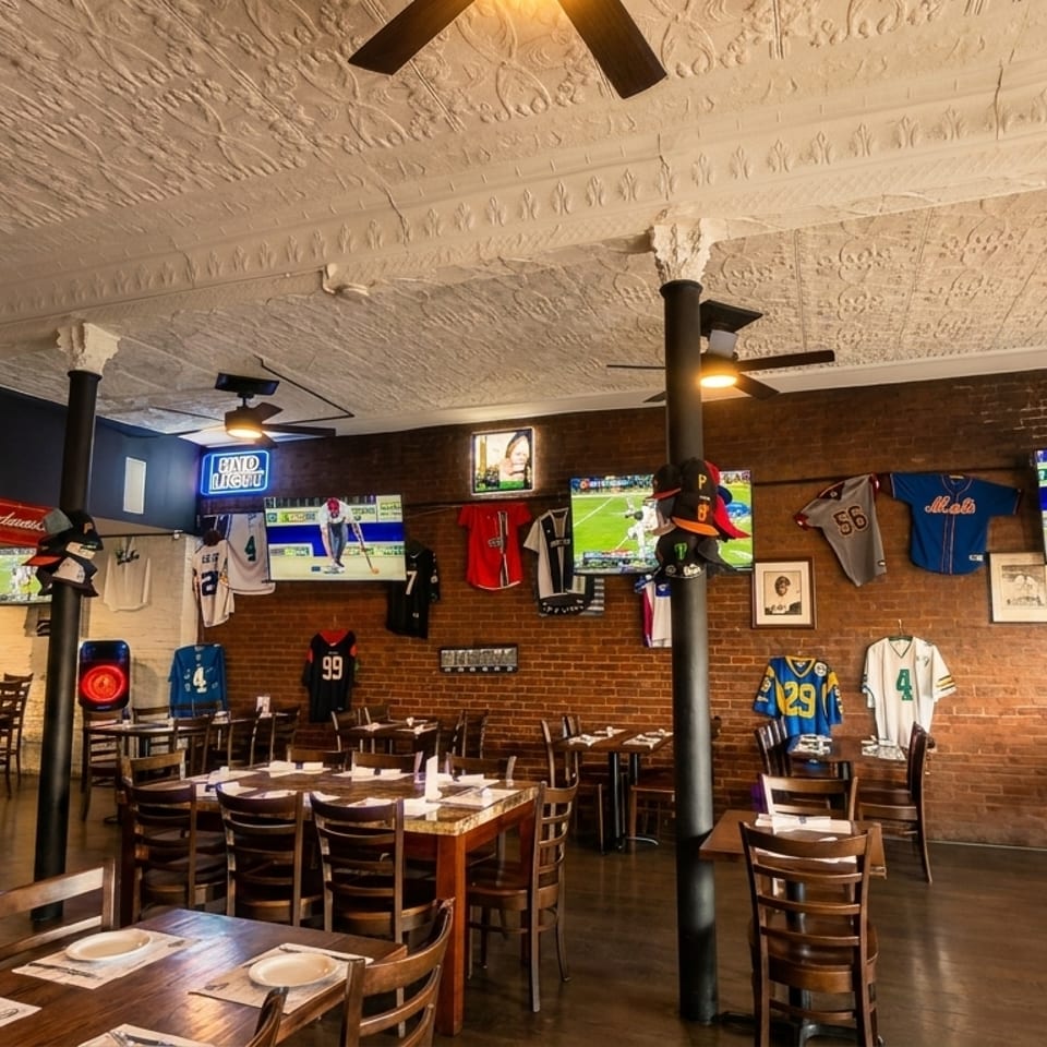 A sports bar interior with brick walls, multiple TVs showing games, and sports jerseys displayed.