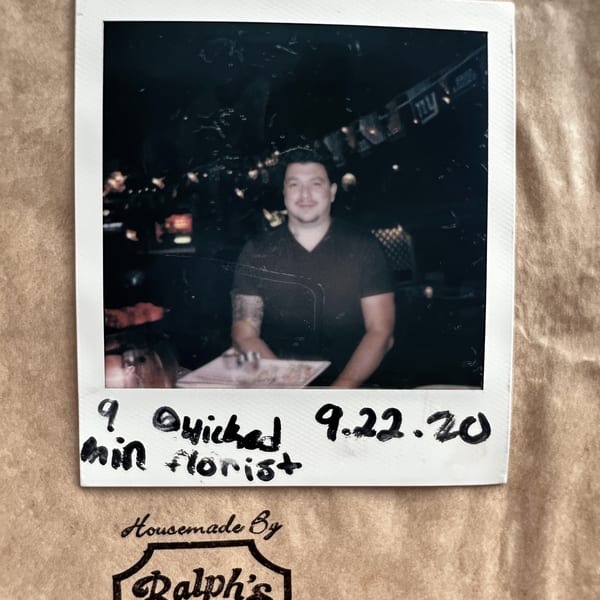 Polaroid of a man with tattoos on his arms, sitting at a table in a dimly lit restaurant.